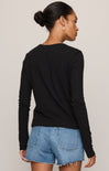 A woman shown from the back wearing a black long-sleeve crewneck top and light blue denim shorts against a plain light gray studio background.