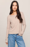 A woman modeling a light beige long-sleeve knit top with a crew neckline, paired with blue jeans, against a solid light gray background.