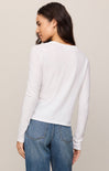 Woman wearing a white sweater and blue jeans against a beige background