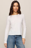 Woman wearing a white long-sleeve top and blue jeans against a beige background
