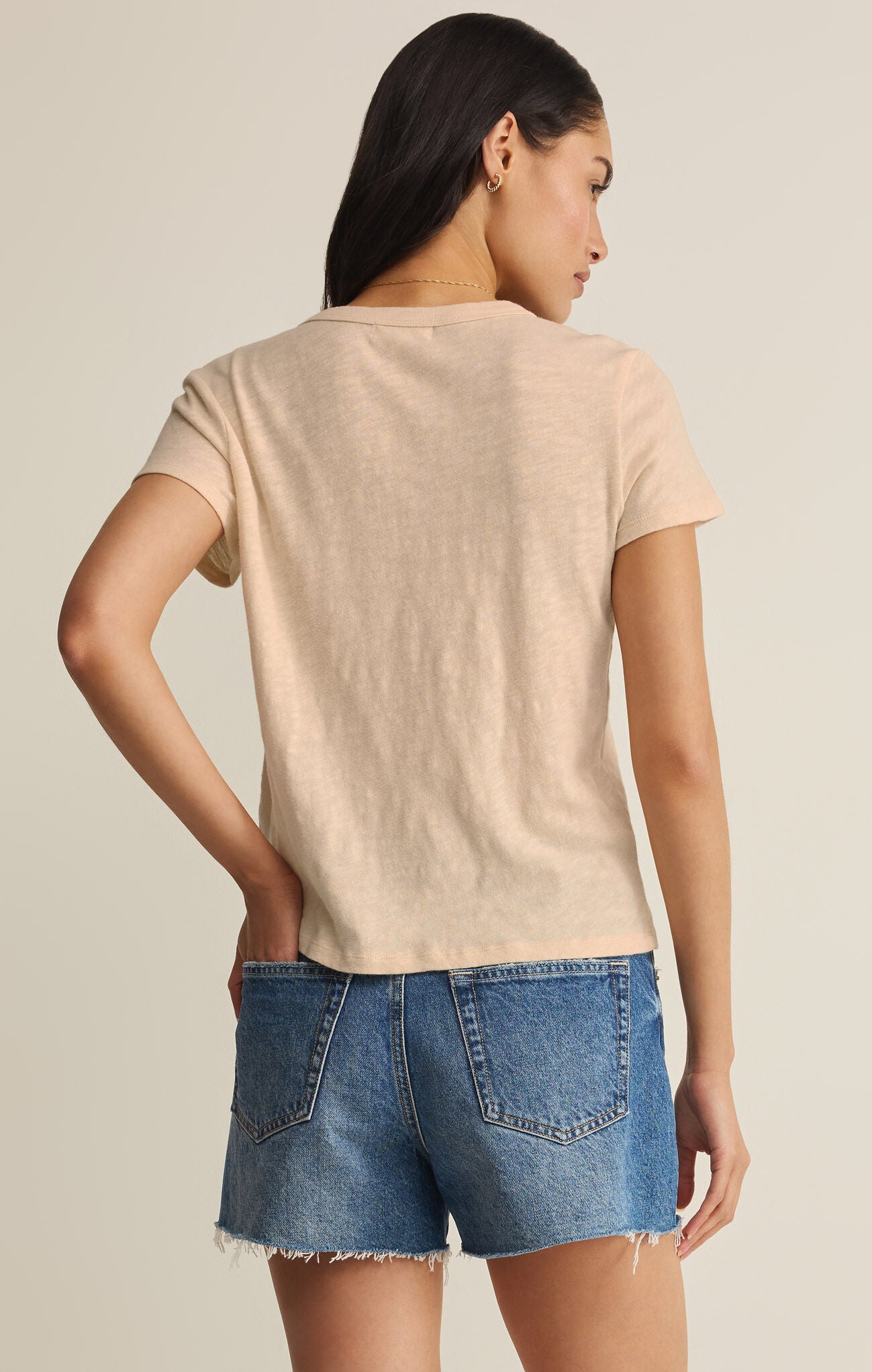 Woman wearing a beige t-shirt and blue denim shorts on a plain background