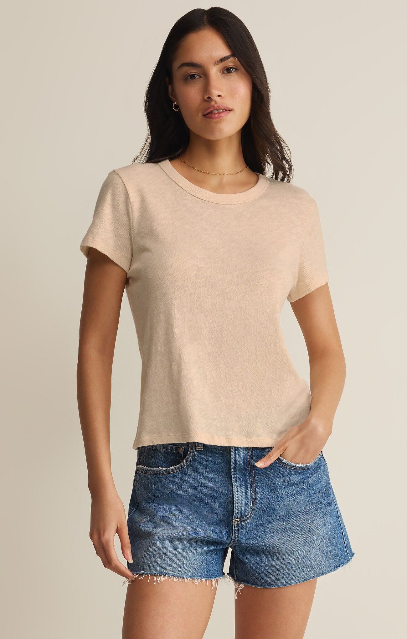 Woman wearing a beige t-shirt and denim shorts on a plain background