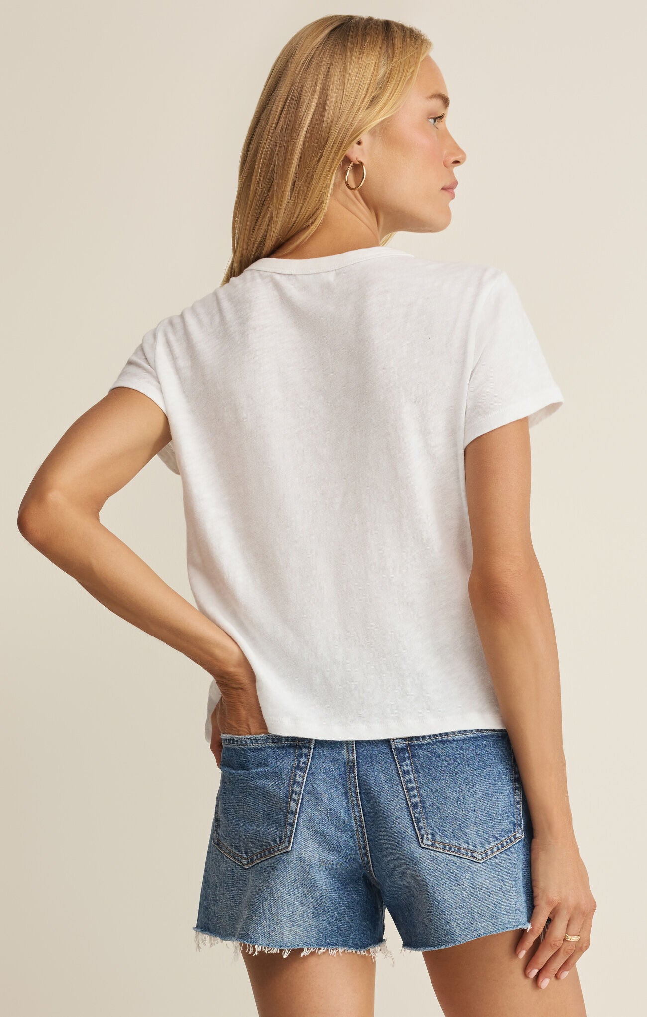 Woman wearing a white t-shirt and denim shorts on a beige background