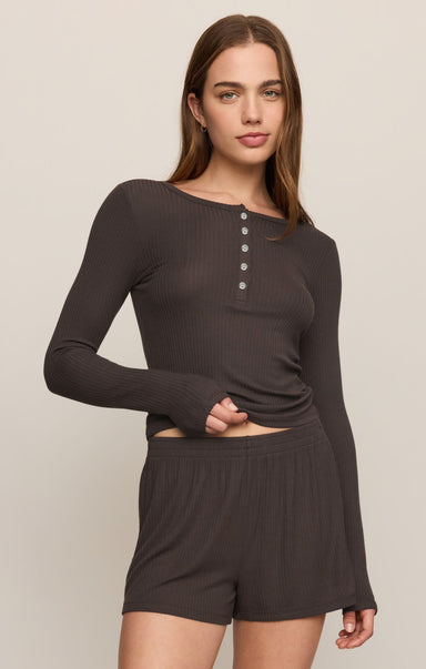 Woman wearing a brown long-sleeve top and shorts on a beige background