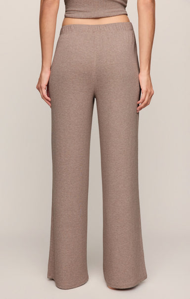 A person wearing high-waisted, wide-leg knit pants in a warm taupe-brown color, shown from the waist down against a plain light beige studio background.