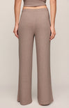 A person wearing high-waisted, wide-leg knit pants in a warm taupe-brown color, shown from the waist down against a plain light beige studio background.
