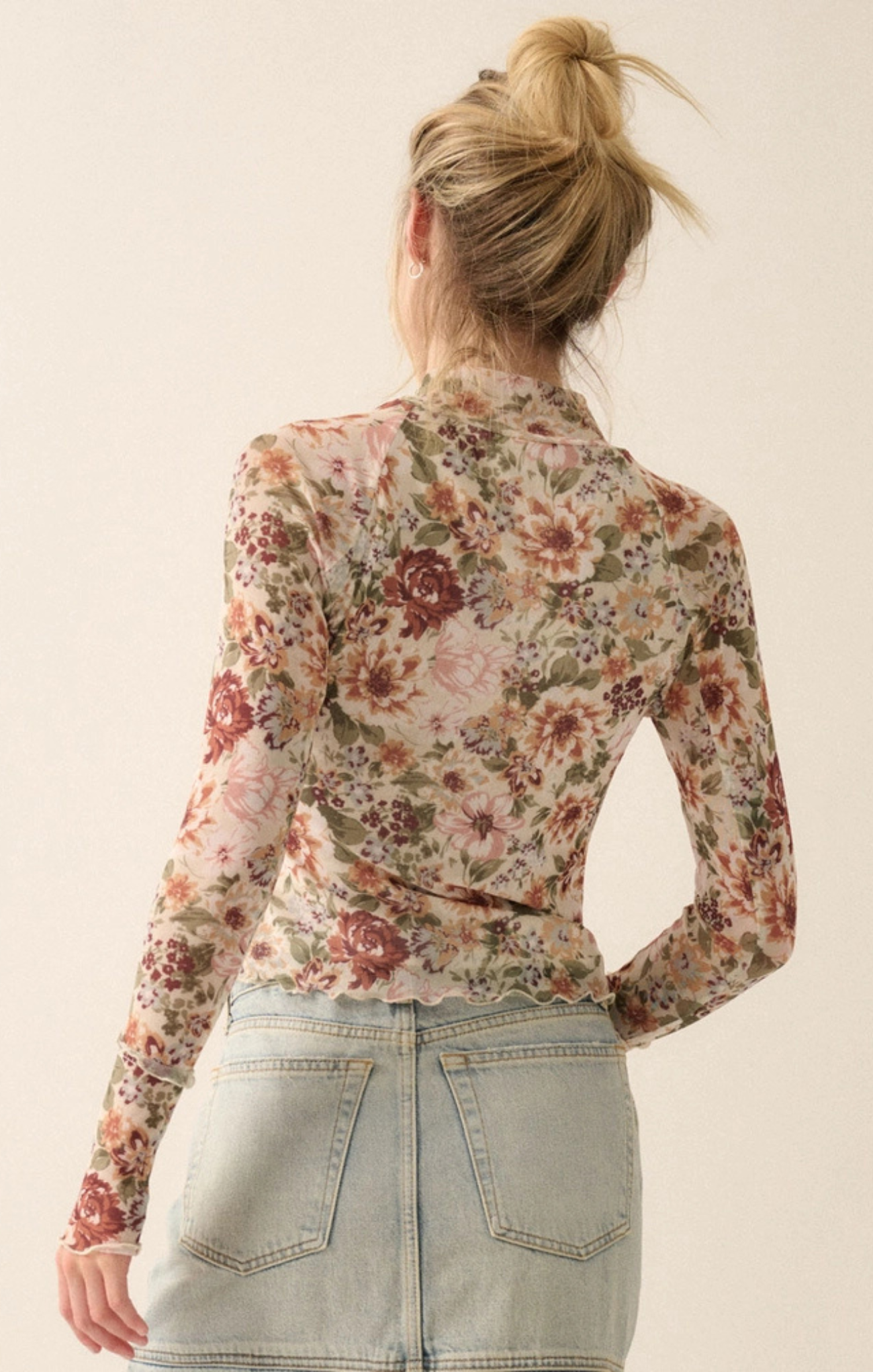 A woman shown from the back wearing a fitted long-sleeve floral blouse with a high neck and light-wash denim skirt against a plain cream background.