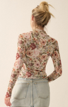 A woman shown from the back wearing a fitted long-sleeve floral blouse with a high neck and light-wash denim skirt against a plain cream background.