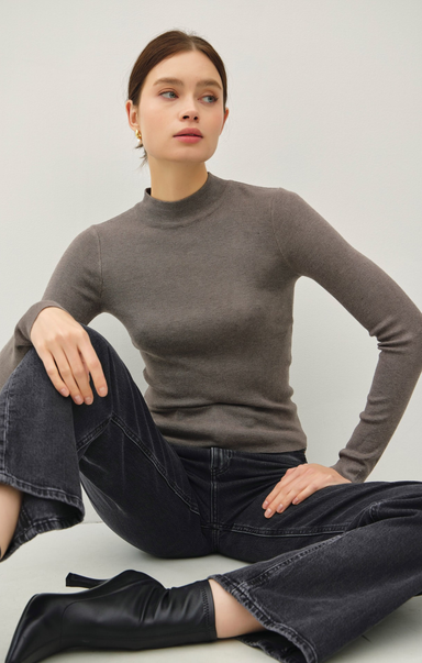 Woman wearing a gray sweater and black pants sitting on a light-colored floor.