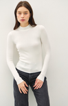 Woman wearing a white turtleneck sweater and dark jeans against a plain background