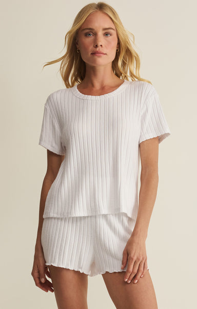 Woman wearing a white ribbed top and shorts set on a beige background