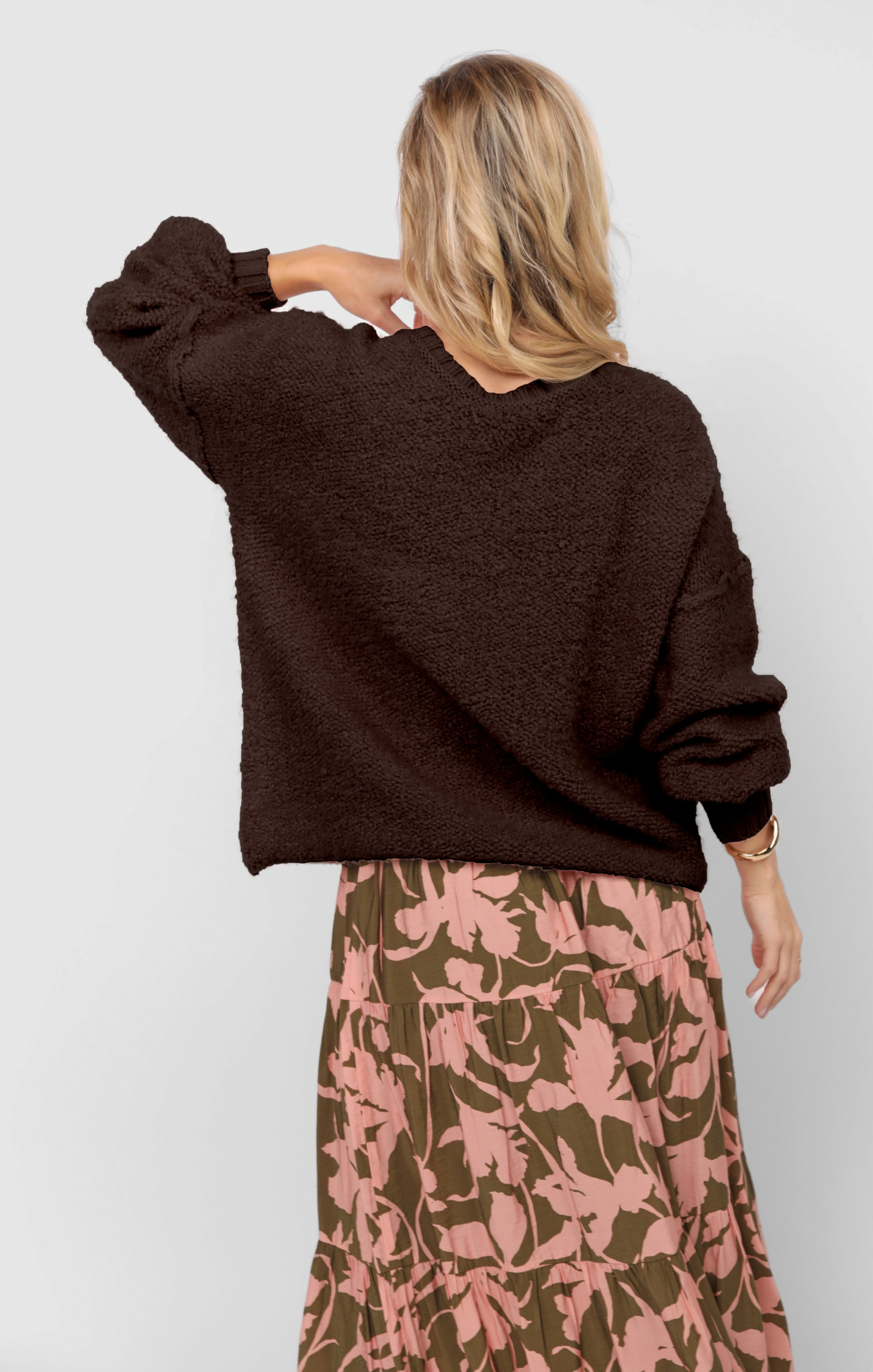 Person wearing a brown sweater and floral skirt on a plain background