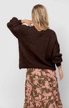 Person wearing a brown sweater and floral skirt on a plain background