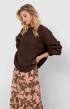 Woman wearing a brown sweater and pink floral skirt on a light gray background