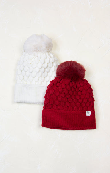 Two knit hats with pom-poms, one white and one red, on a light background.