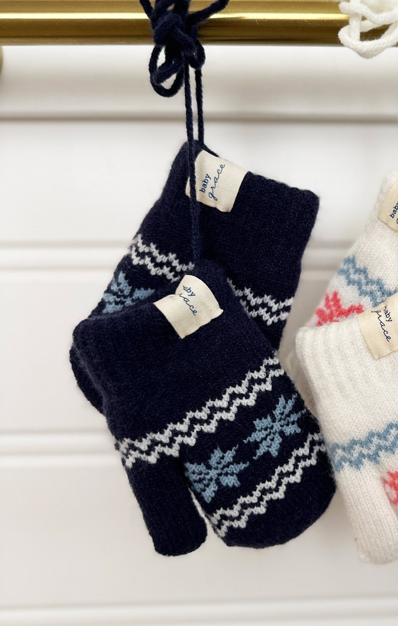 Pair of navy blue knitted mittens with white patterns hanging on a white surface.