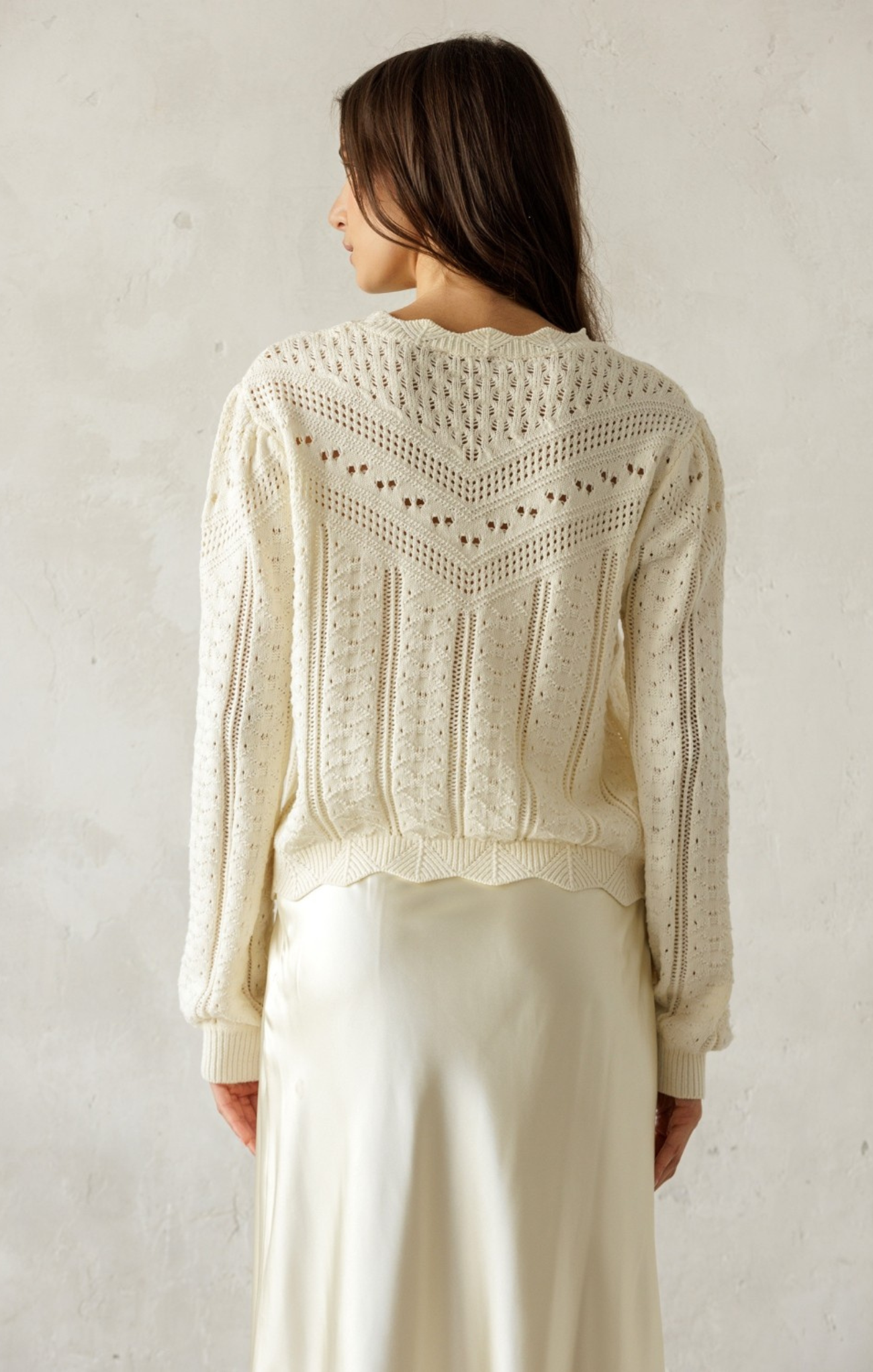 Woman wearing a cream-colored knit sweater against a plain background