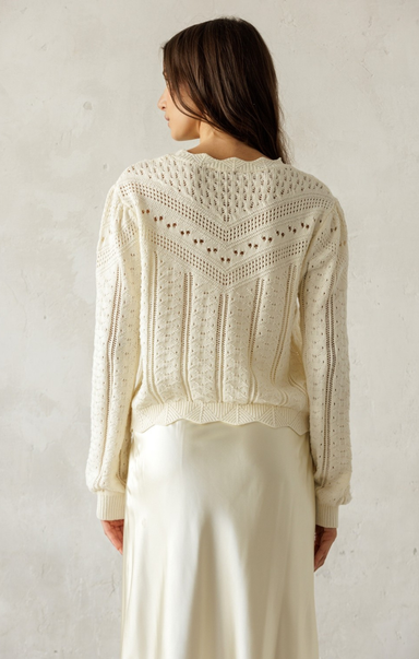 Woman wearing a cream-colored knit sweater against a plain background