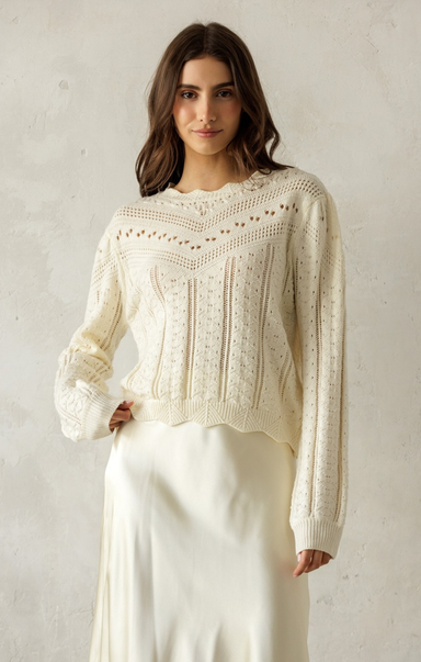 Woman wearing a cream-colored knit sweater against a plain background
