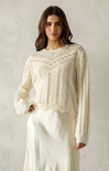 Woman wearing a cream-colored knit sweater against a plain background