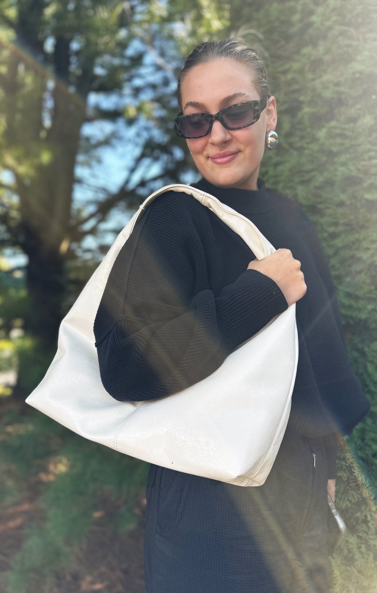 Woman holding a white tote bag outdoors with trees in the background
