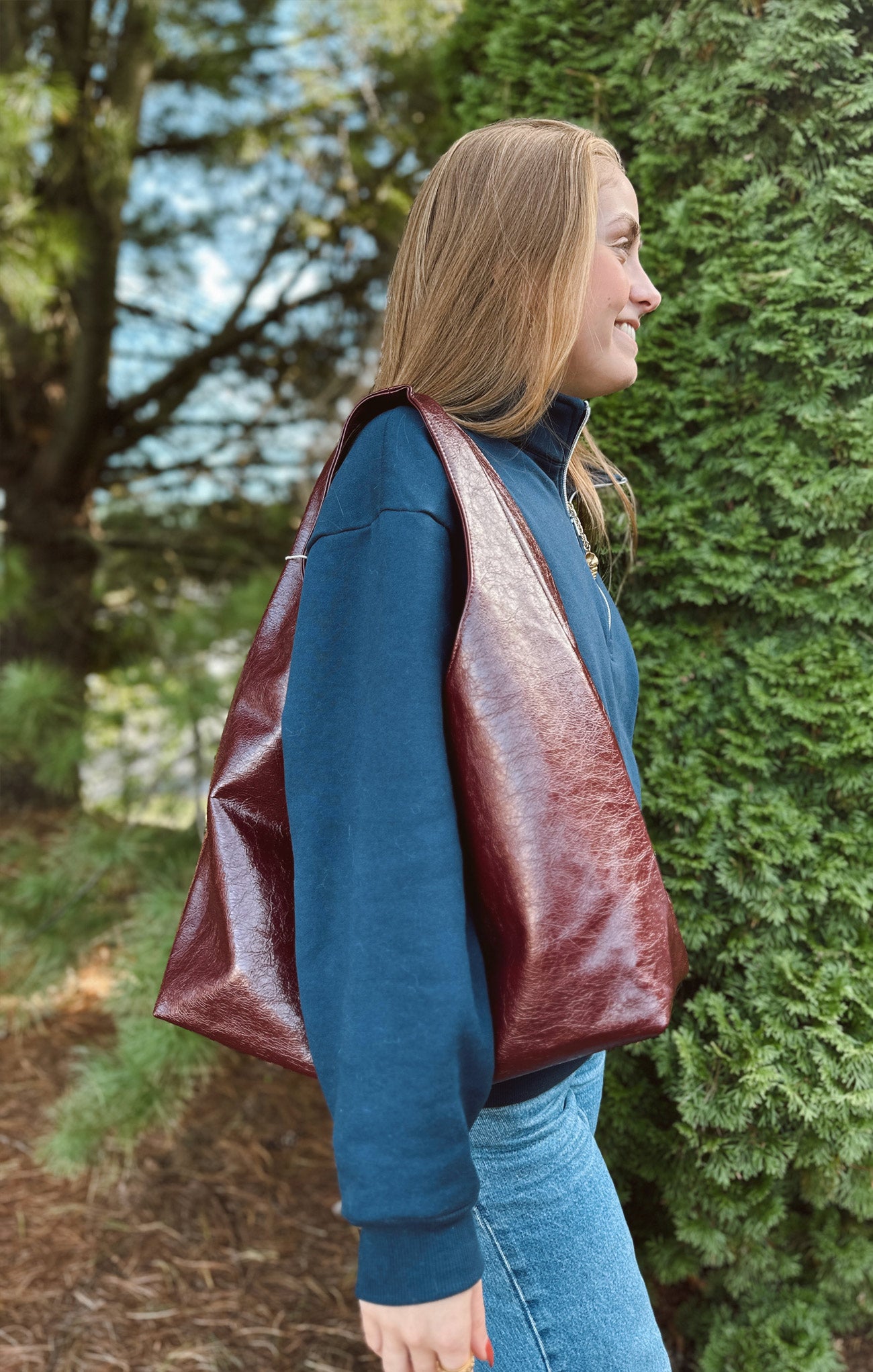 Woman wearing a blue jacket with a red leather vest over it, standing outdoors.