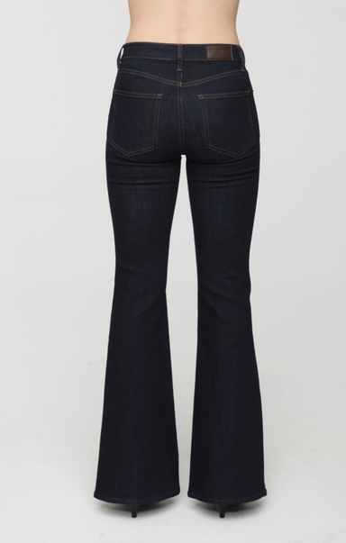 Rear view of a person wearing dark indigo flare jeans with a brown leather waistband patch, standing against a light gray studio background.