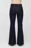 Rear view of a person wearing dark indigo flare jeans with a brown leather waistband patch, standing against a light gray studio background.