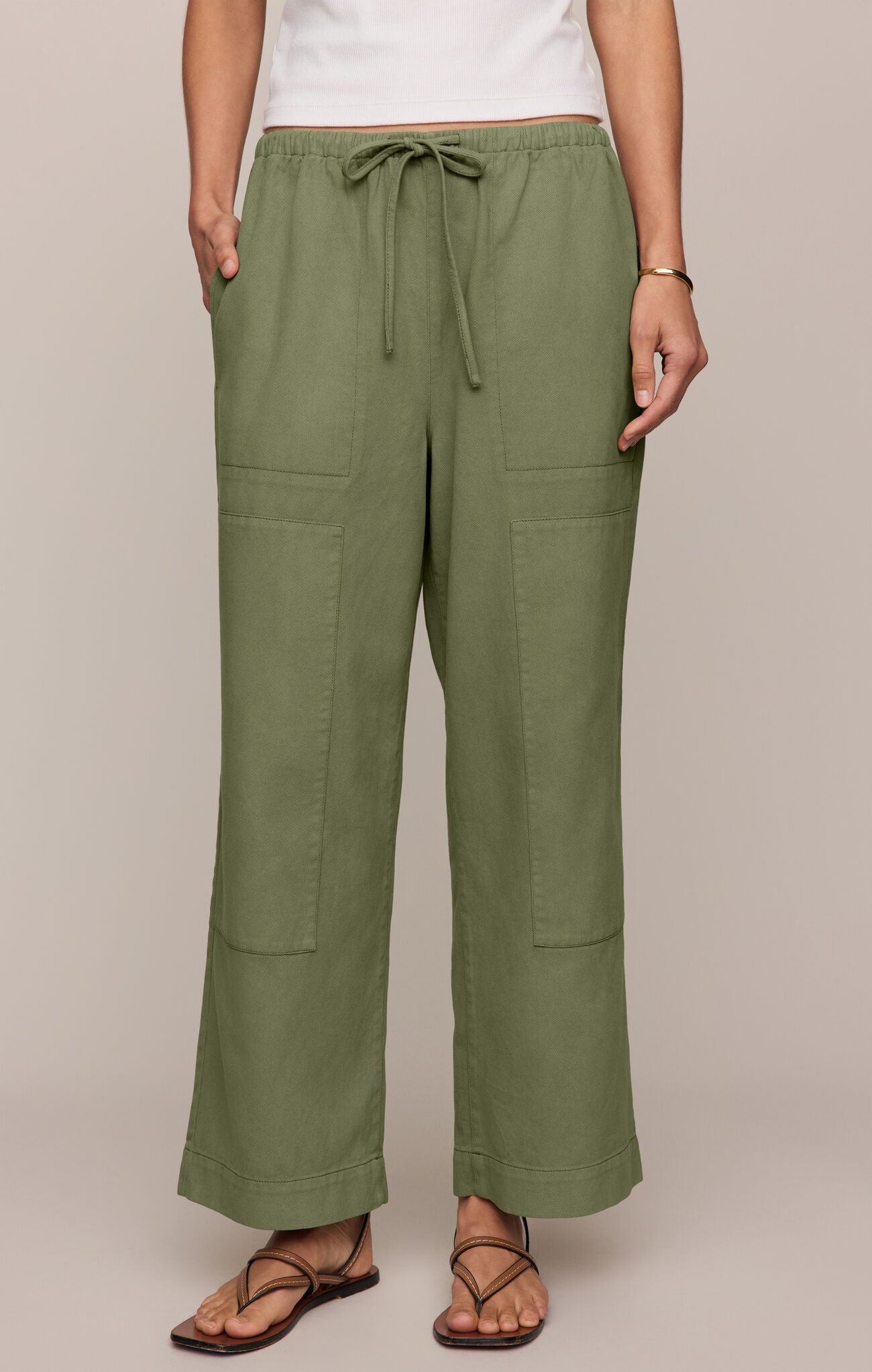 Person wearing olive green pants with a drawstring waist on a plain background