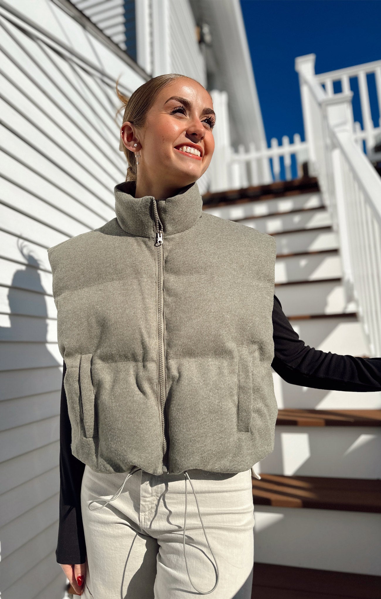 Woman wearing a gray puffer vest standing on a staircase with a white railing.