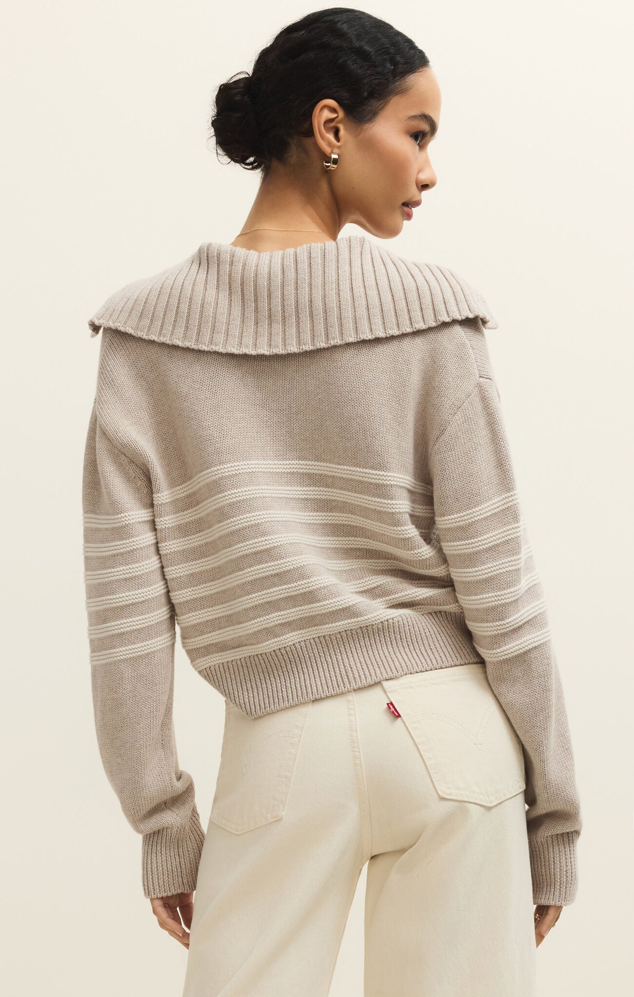 Woman wearing a beige sweater with a textured collar against a plain background