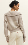 Woman wearing a beige sweater with a textured collar against a plain background