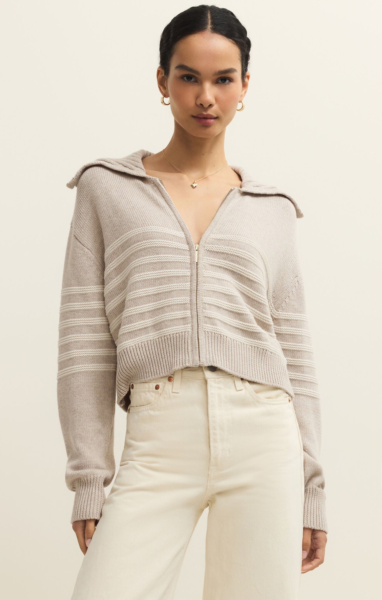 Woman wearing a light gray zip-up sweater with a neutral background