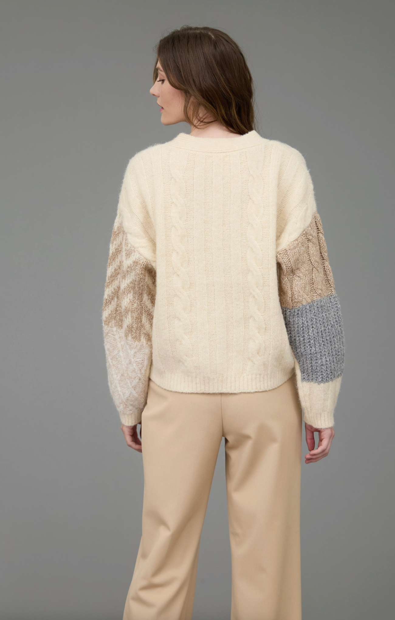 Woman wearing a cream sweater with patterned sleeves against a gray background