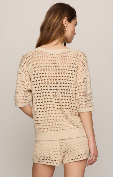 Woman wearing a beige crochet outfit on a plain background