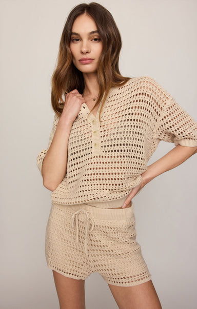 Woman wearing a beige crochet top and shorts set against a plain background
