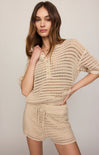 Woman wearing a beige crochet top and shorts set against a plain background