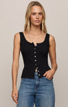 Woman wearing a black sleeveless top with buttons and blue jeans on a beige background