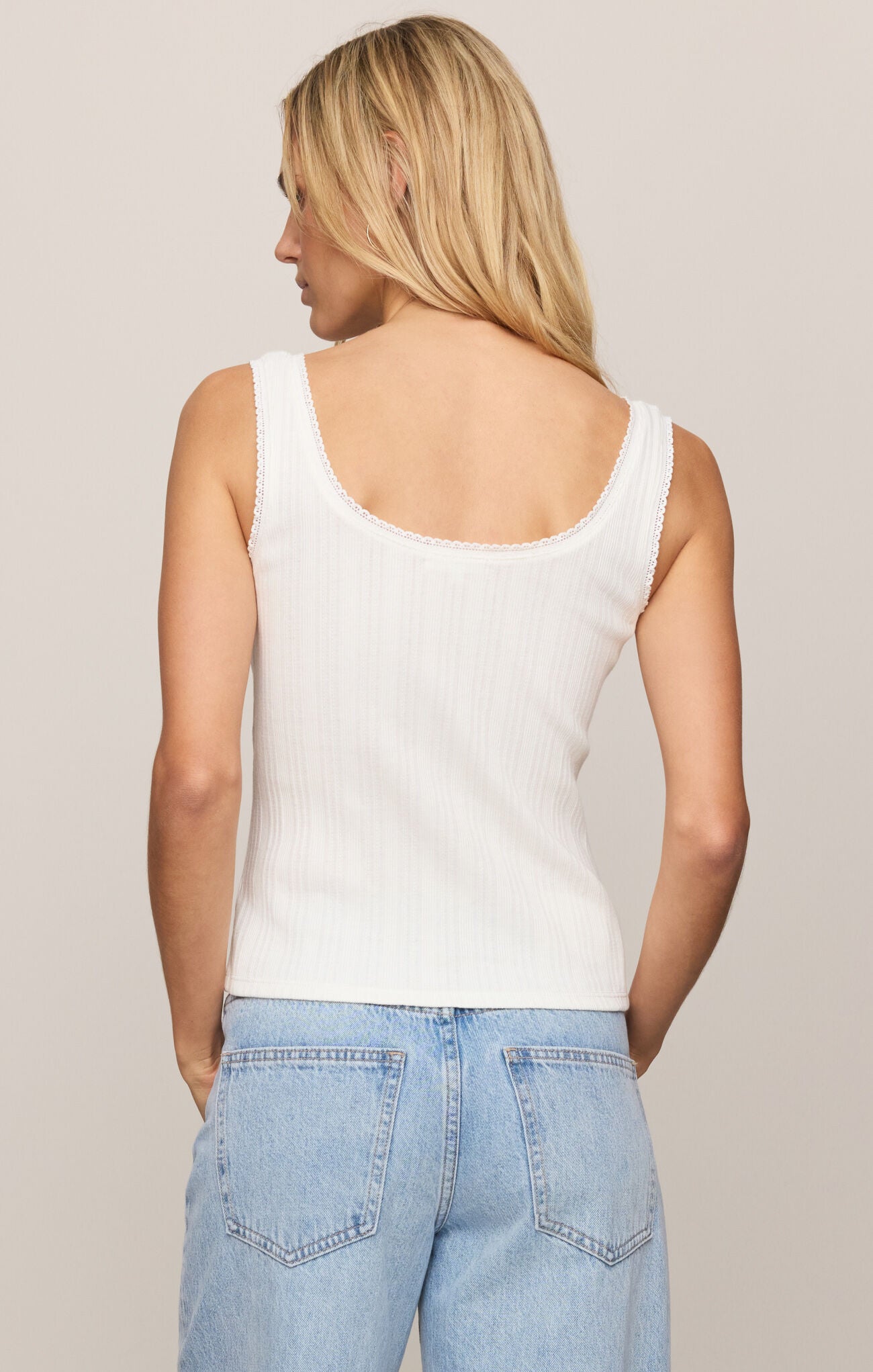 Woman wearing a white tank top and light blue jeans against a beige background