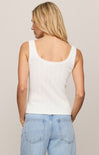 Woman wearing a white tank top and light blue jeans against a beige background