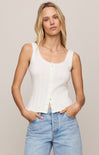 Woman wearing a white sleeveless top and light blue jeans against a plain background