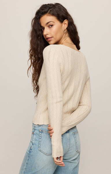 Woman wearing a cream sweater and light blue jeans against a plain background