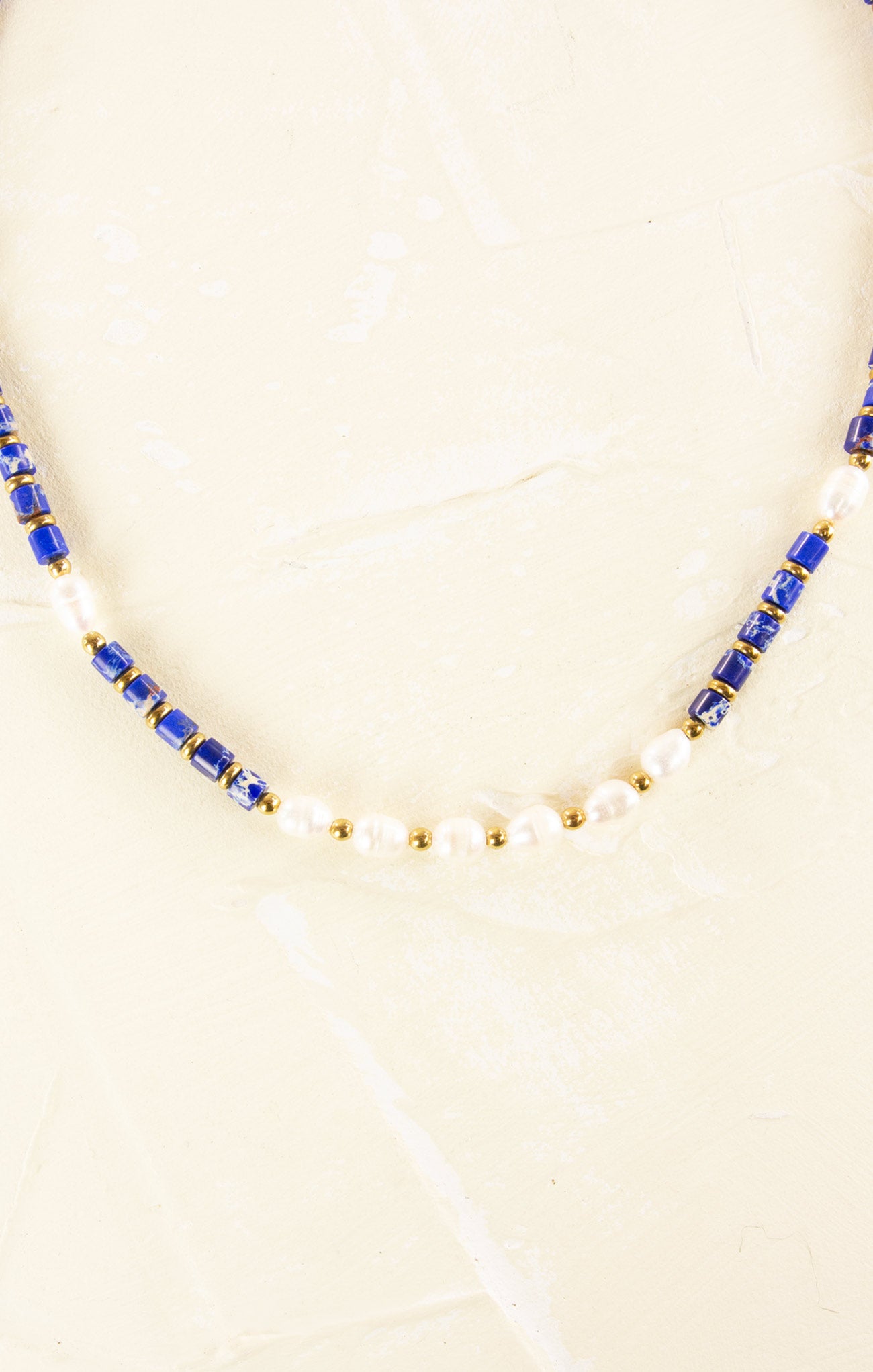Necklace with blue and gold beads on a beige background
