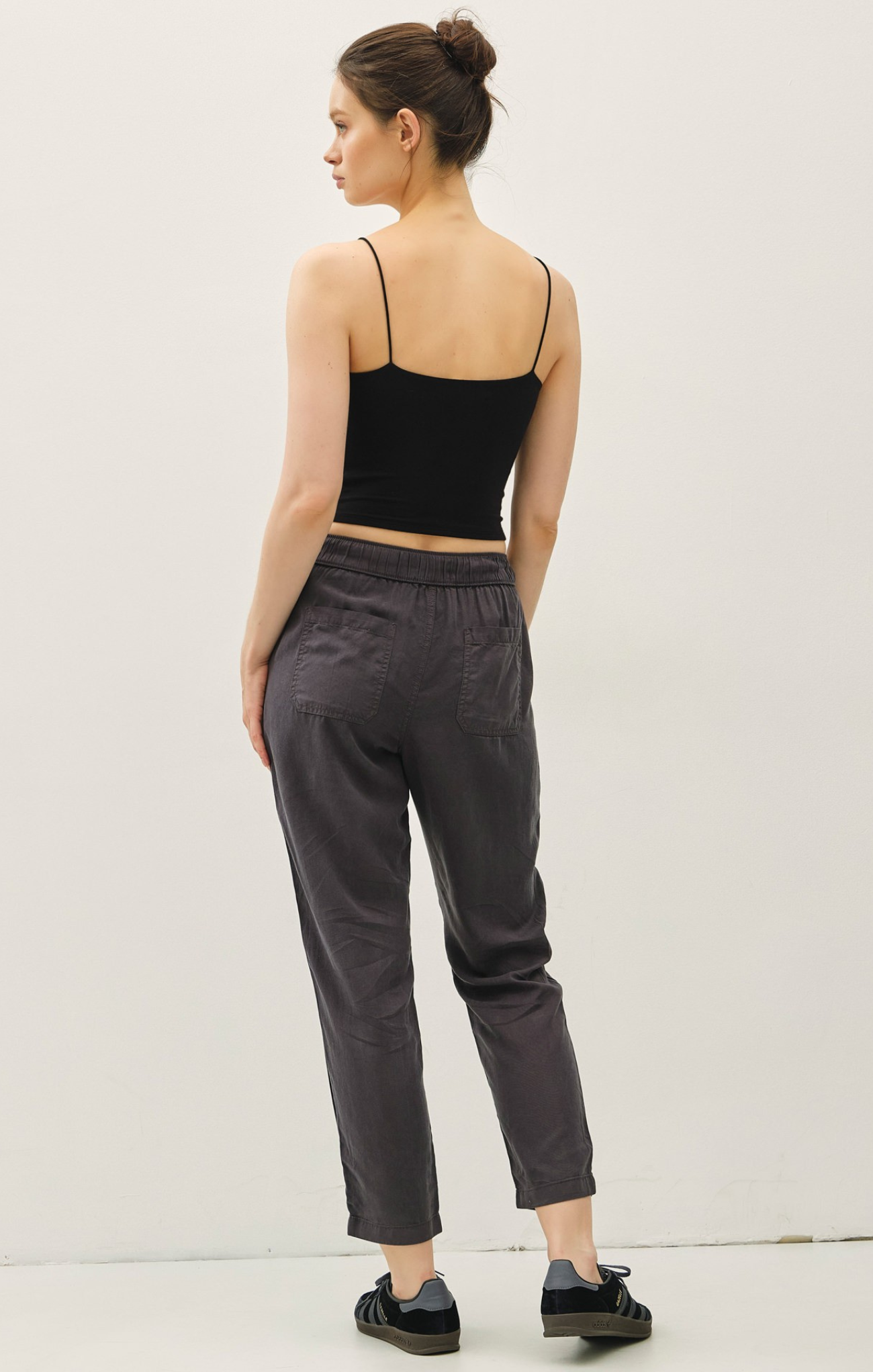 Woman wearing a black top and gray pants against a white background