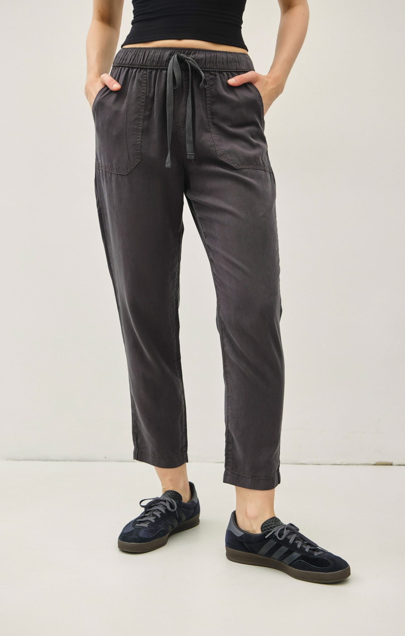 Person wearing dark gray pants with a drawstring waist against a white background