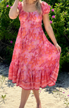 Woman wearing a pink floral dress standing outdoors with greenery in the background