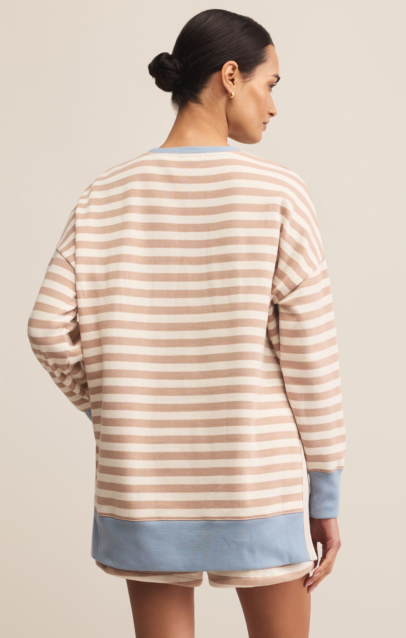 A woman wearing a beige and light blue striped sweatshirt with a crew neck. The sweatshirt has long sleeves and a relaxed fit.