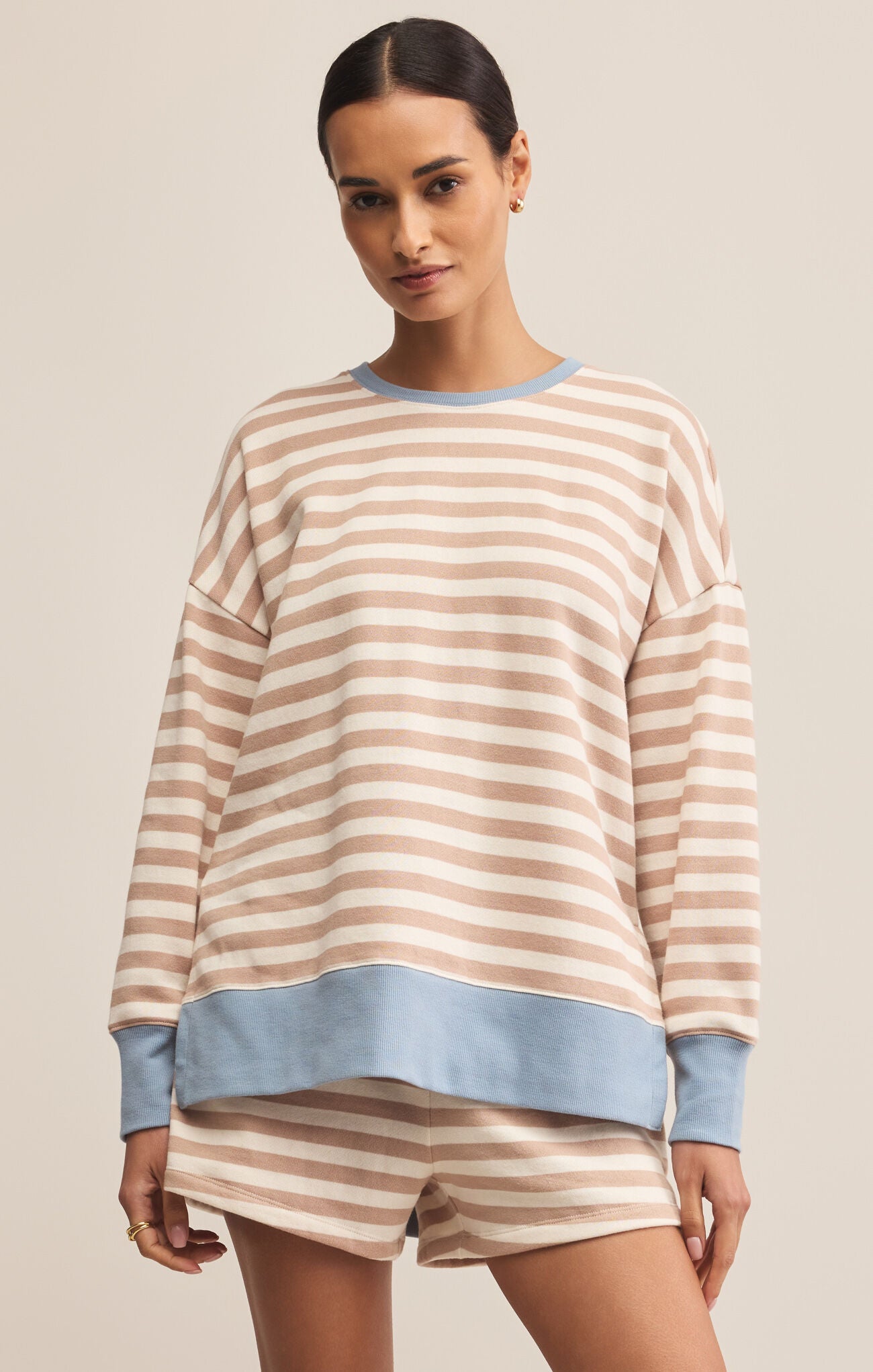 A woman wearing a beige and light blue striped sweatshirt with a crew neck. The sweatshirt has long sleeves and a relaxed fit.