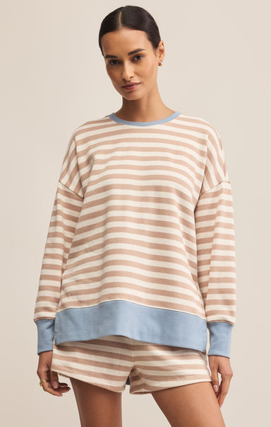 A woman wearing a beige and light blue striped sweatshirt with a crew neck. The sweatshirt has long sleeves and a relaxed fit.