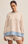 A woman wearing a beige and light blue striped sweatshirt with a crew neck. The sweatshirt has long sleeves and a relaxed fit.